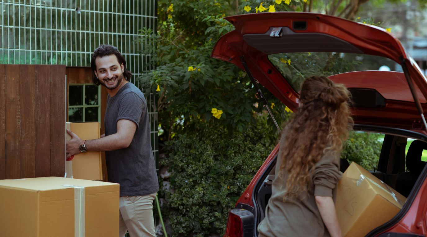 A couple unloading moving boxes from a car outside their new home